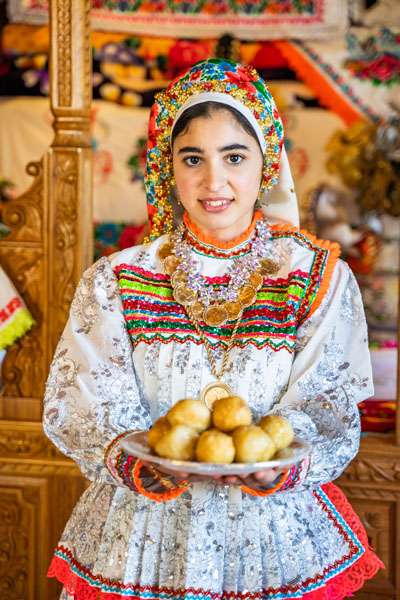 Young lady dressed in traditional while Olympos dress offering loukoumades.